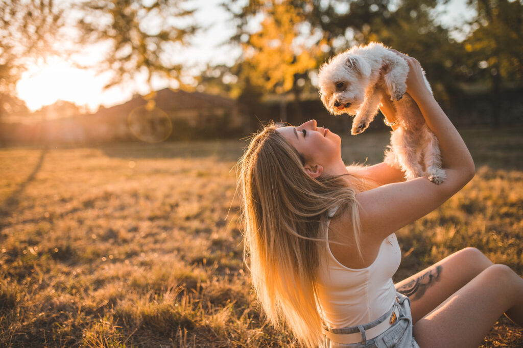 Une femme qui porte son petit chien dans un parc naturel
